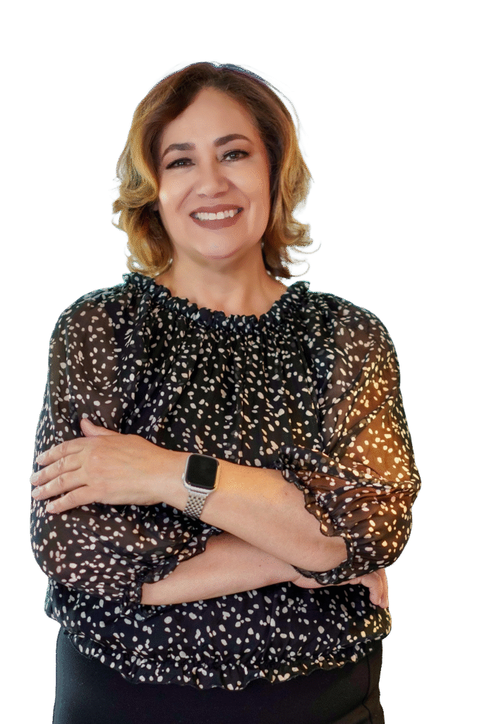 A woman with wavy, shoulder-length hair smiles confidently with arms crossed, wearing a black polka dot blouse and smartwatch. She stands against a plain background, representing reliable Mobile Notary Services New Jersey.