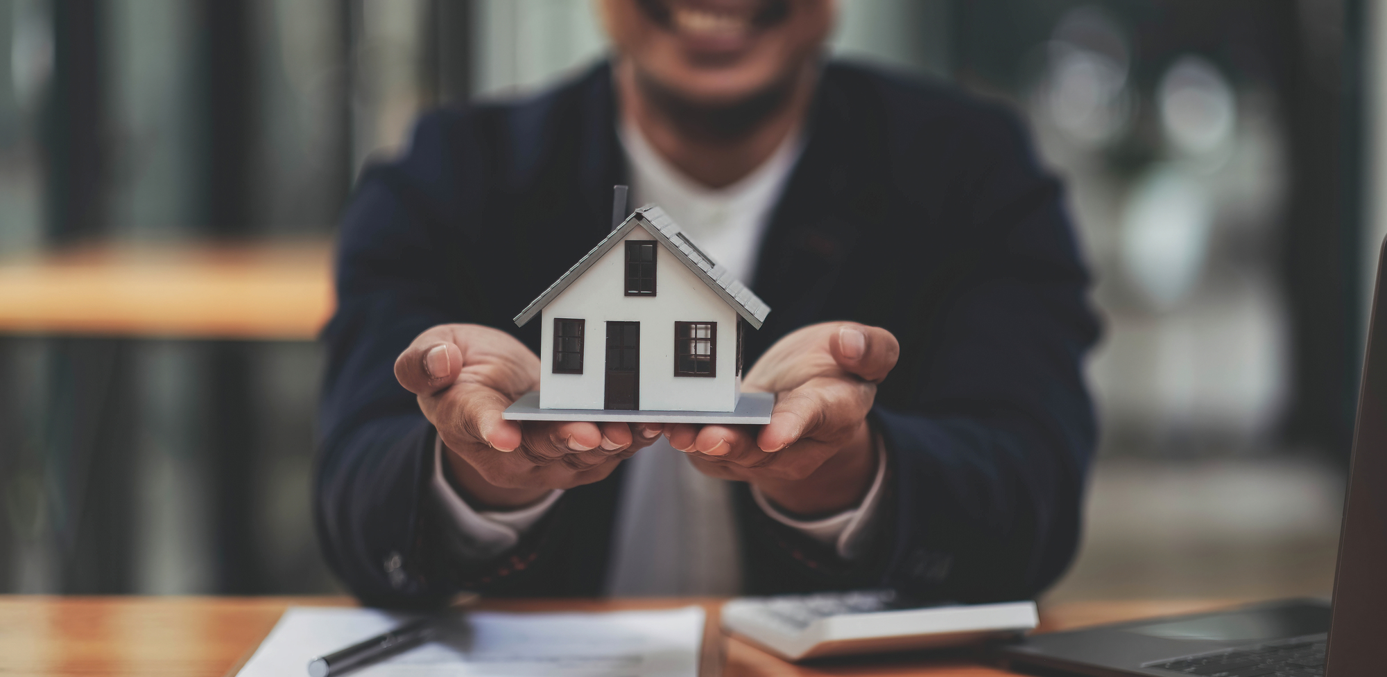 Close-up of smiling man holding a model house with loan documents and calculator on table — symbolizing home loan notary services in New Jersey