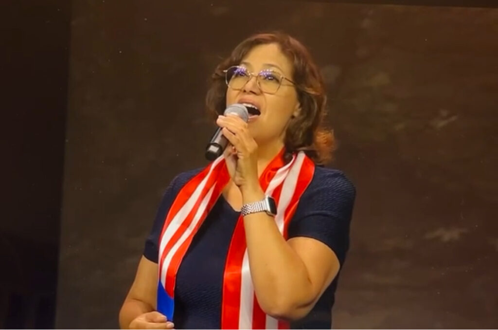 Hispanic female notary speaking at a patriotic event with American flag scarf